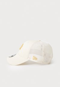 Cremefarvet baseballkasket med netbaggrund, med gult broderet logo på fronten og siden. Bøjet skygge og justerbar rem bagpå.