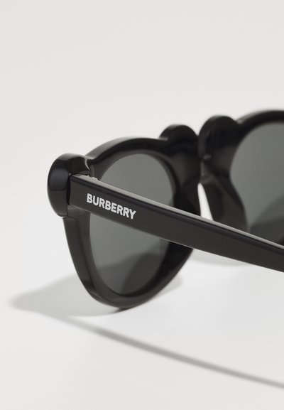 Crne sunčane naočale s okruglim staklima i sjajnim završetkom. Okvir ima jedinstven oblik, s "Burberry" logotipom sa strane.
