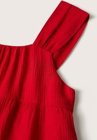 Robe rouge sans manches avec larges bretelles et détail en tissu texturé froncé sur un fond clair uni.