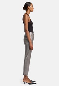 Zilverkleurige metallic aansluitende broek met een middelhoog taille, zijzakken en een strakke afwerking, gecombineerd met zwarte puntige muilkorven en een aansluitende zwarte tanktop.