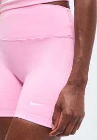 Gros plan d'une personne portant un short de sport Nike rose clair avec un logo swoosh blanc sur la cuisse gauche et un haut rose assorti.