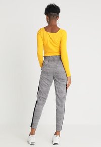 Gul ribbad långärmad tröja i kombination med grå rutiga tapered-byxor med svarta sidostreck. Modellen har på sig vita sneakers.