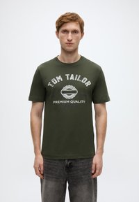 Πράσινο ελιάς βαμβακερό T-shirt με στρογγυλή λαιμόκοψη, κοντά μανίκια και λευκό τυπωμένο λογότυπο "TOM TAILOR" και "PREMIUM QUALITY" στο μπροστινό μέρος.