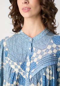 Blåmønstret bluse med knapkrave, fremhævet af rynket tekstur og et ternet design i varierende nuancer af blå og creme.