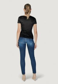 Sort tætsiddende kortærmet top og mørkeblå jeans med skræddersyet pasform, parret med nøgne højhælede sko. Har en glat tekstur og diskrete detaljer.