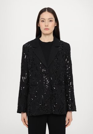 Blazer nero con paillettes e un motivo a foglia testurizzato, con rever a scollo a V e due tasche frontali, indossato sopra un top nero.