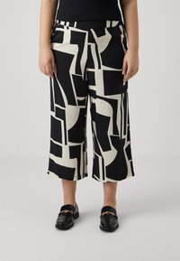 Pantalons large à motifs noir et blanc avec des formes géométriques, en tissu léger. Devant plat avec poches et coupe décontractée.