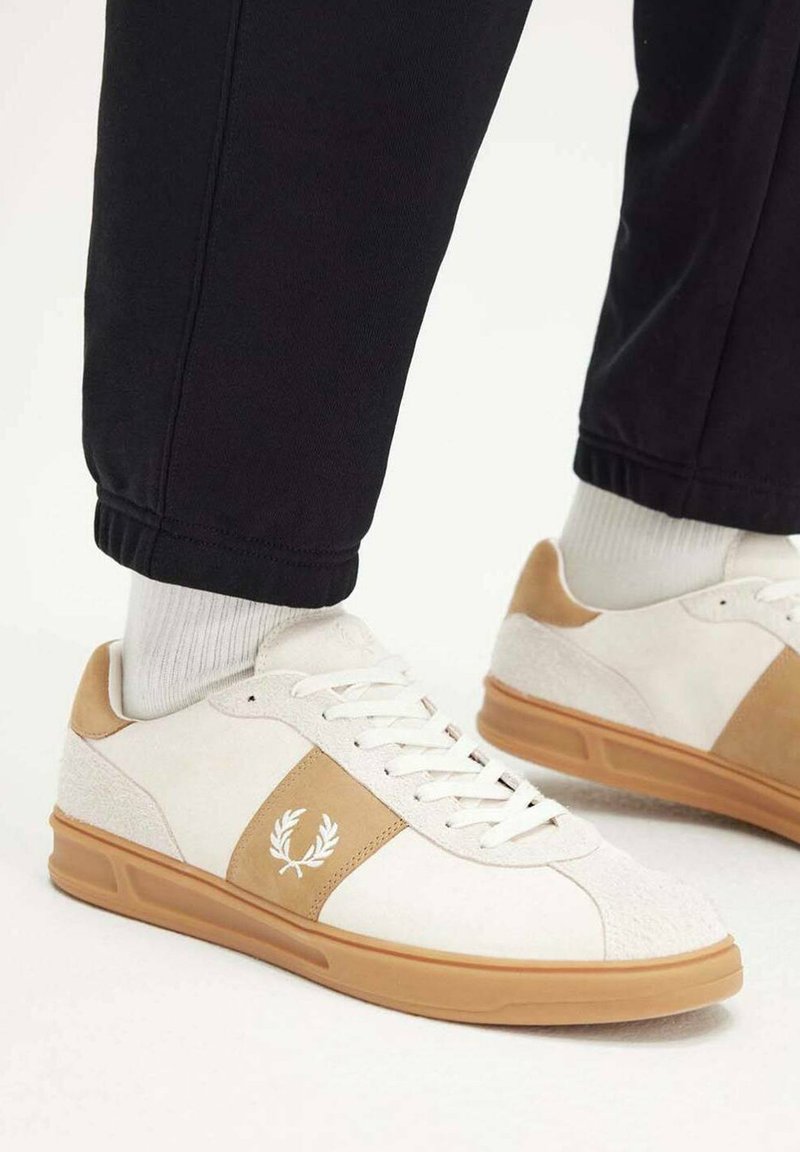 Zapatillas deportivas blancas con acentos de ante marrón, paneles texturizados y cordones blancos. Suela de goma con marca en el lateral.