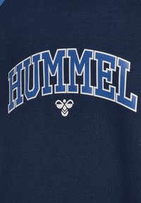 Granatowa bawełniana bluzka z kapturem z napisem "HUMMEL" w wyraźnym białym i jasnoniebieskim kolorze, z małym logo pszczoły poniżej tekstu.