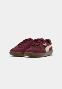 Burgundowe zamszowe sneakersy z kremowymi akcentami, okrągły nosek, teksturowana gumowa podeszwa oraz wiązany design, z logo na boku.