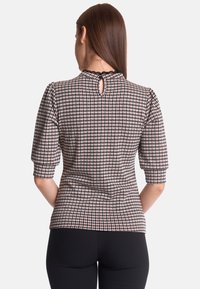 Figursydd blus i texturerat svart, vitt och rött hundtandsmönster. Har korta puffärmar och ett nyckelhål i ryggen.