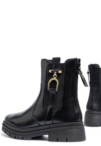 Black leather ankle boots featuring a zip closure, elastic side panels, chunky rubber sole, and gold accent hardware on the pull tab.