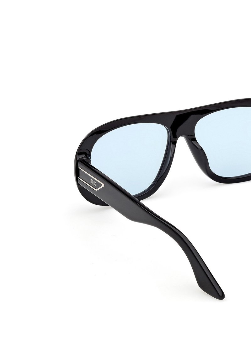 Lunettes de soleil noires surdimensionnées avec des verres teintés bleu clair et un logo "GCDS" sur la branche, présentées en angle sur un fond blanc.