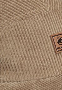 Brun kordfløyelskeps med vertikal ribbing, med en teksturert overflate og en lærflekk som viser en logo.