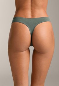 Zeleni bombažni tangice z gladko, raztegljivo teksturo. Imajo minimalno pokritost in preprosto zasnovo pasu.