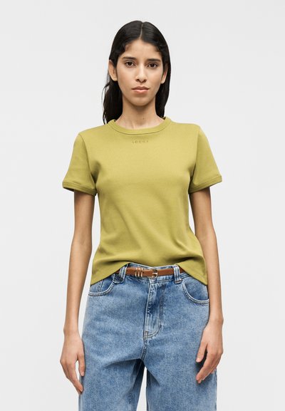 Πράσινο ελιάς εφαρμοστό μπλουζάκι με κοντά μανίκια και στρογγυλή λαιμόκοψη, με διακριτικό τυπωμένο κείμενο. Συνδυασμένο με ανοιχτό μπλε τζιν παντελόνι και καφέ ζώνη.