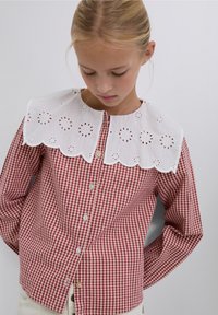Red and white gingham shirt with a scalloped, embroidered white collar. Button front and long sleeves with fitted cuffs.