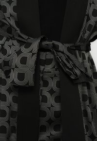 Must kleit, millel on valgete geomeetriliste joontega must mustriline kangas, millel on vöökohal samast kangast vöö.