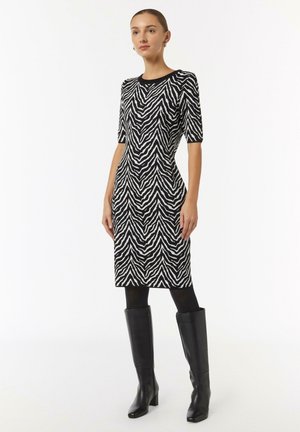 Schwarz-weiß gestreiftes Strickkleid im Zebra-Muster mit kurzen Ärmeln, Rundhalsausschnitt und mittellanger Schnittform, kombiniert mit kniehohen schwarzen Stiefeln.