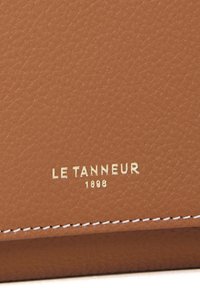Portafoglio in pelle marrone con superficie texture, logo in rilievo dorato "LE TANNEUR 1898" e cuciture bianche lungo il bordo.