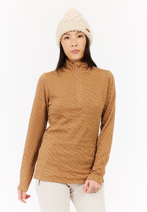 Brun langærmet pullover med halvlukning og tekstureret bølgemønster. Modellen bærer en cremefarvet strikket hue med en pom-pom på toppen.