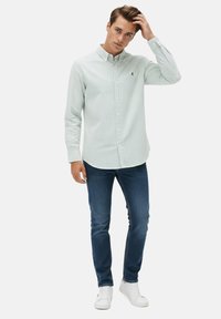 Camisa de manga larga a rayas verdes claras y blancas con cuello abotonado, combinada con vaqueros azul oscuro y zapatillas blancas.