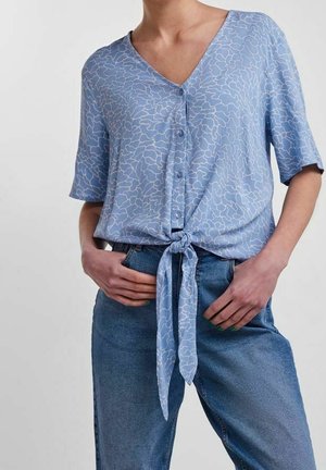 Lichtblauwe kortermige blouse met V-hals, knopen aan de voorkant en een geknoopt strikdetail in de taille, met een subtiel abstract wit patroon.