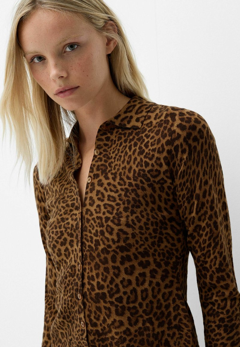 Leopardenmuster-Hemd in Braun und Beige, mit Kragen, langen Ärmeln und einer weichen Textur. Die Knöpfe sind an der Vorderseite sichtbar.