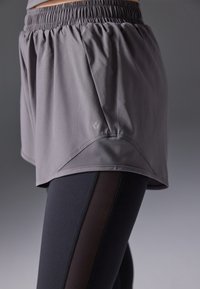 Harmaat, kevyet juoksushortsit, joissa on joustava vyötärönauha, taitettu helma ja sivulla logo. Yhdistetty mustiin legginsseihin, joissa on sivusomisteet.