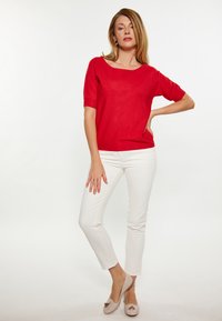 Punainenshort-sleeve villapaita, jossa on leveä kaula-aukko, yhdistettynä valkoisiin slim-fit-housuihin ja nudenvärisiin korkeakorkoisiin kenkiin, joissa on koristeellinen yksityiskohta.