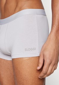 Boxer brevi SLOGGI grigi realizzati in tessuto morbido e elastico, con un orlo liscio e un discreto logo sulla coscia. Vista ravvicinata.