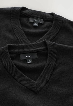 Svarta v-ringade tröjor staplade, med ribbade kragar. Etiketter visar märket "NEXT," storlek "M," och "Tillverkad i Bangladesh." Mjuk textur är märkbar.