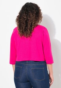 Sweatshirt court, rose vif, avec des manches trois-quarts et un col rond, associé à un jean en denim foncé avec des poches arrière.