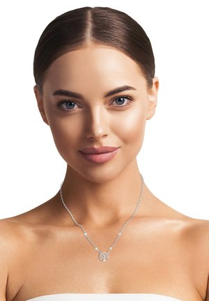 Silberne Halskette mit rundem Anhänger, der detaillierte Ausschnitte aufweist und mit Perlen an einer zarten Kette verziert ist. Das Modell trägt sie vor einem neutralen Hintergrund.