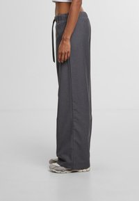 Grijze, wijde broek met een trekkoord in de taille, een gladde textuur en een losse pasvorm, gecombineerd met lichtgekleurde sneakers.