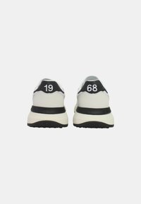 Zapatillas con una parte superior de cuero blanca, acentos negros en el talón y números en relieve "19" y "68" en la parte trasera, con una gruesa suela blanca.