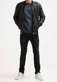 Svart läderbombarjacka över en marinblå stickad tröja, svarta skinny jeans och vita sneakers. Texturerad tyg och åtsittande design.