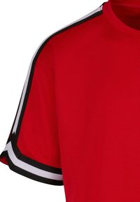 Tricou sportiv roșu dintr-un material respirabil din plasă. Prezintă dungi alb-negre pe mâneci și un guler rotund.