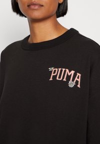 Czarna bluza z okrągłym dekoltem i kolorowym logo "PUMA" z kwiatowymi oraz pszczelimi zdobieniami na klatce piersiowej. Miękka tekstura.