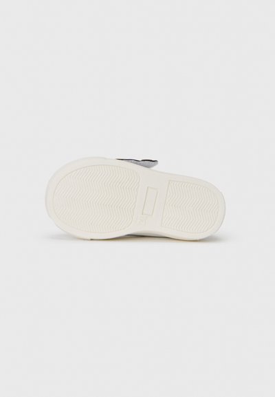 Semelle blanche en caoutchouc d'une chaussure avec un motif de semelle en chevrons, dotée d'une sangle en tissu doux de couleur grise, ornée d'un accent contrastant.