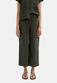 Zielony, luźny top z krótkim rękawem w połączeniu z szerokimi spodniami w tym samym kolorze, wykonanymi z lekkiego materiału. Dopełnieniem stroju są sandały na obcasie.
