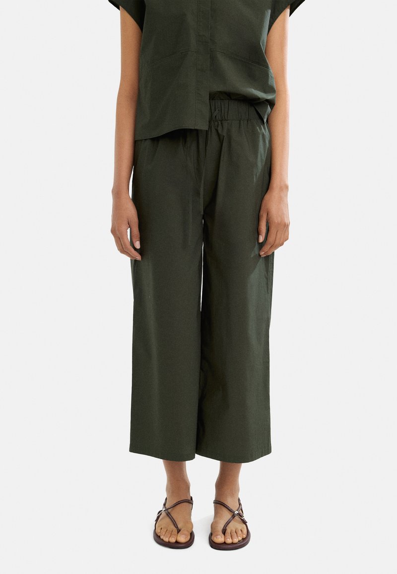 Zielony, luźny top z krótkim rękawem w połączeniu z szerokimi spodniami w tym samym kolorze, wykonanymi z lekkiego materiału. Dopełnieniem stroju są sandały na obcasie.