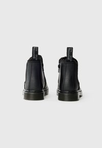 Botas de tornozelo pretas com um exterior de couro liso, forro macio e um fecho éclair. Apresenta uma sola texturizada preta e alças de puxar com letras brancas.