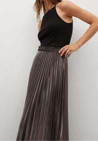Zwarte mouwloze top gecombineerd met een geplooide, metallic bronzen maxi-rok met een elastische tailleband en een soepele, vloeiende textuur.