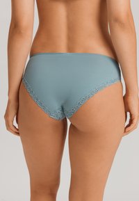 Světle modrý bavlněný bikini s krajkovým lemem. Vyznačuje se hladkým materiálem a dekorativním vlnitým okrajem kolem pasu a nohaviček.
