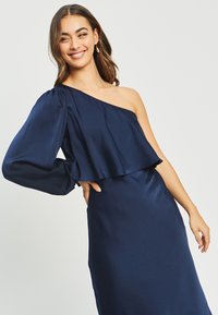 Navy satin dress with one long sleeve and an asymmetrical neckline. The top features a flowing overlay, creating a layered effect.