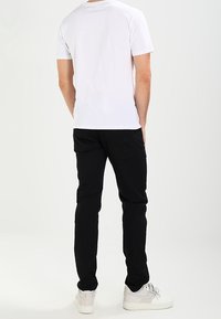 Camiseta blanca de manga corta, pantalones negros y zapatillas blancas. La tela parece suave; los pantalones tienen un diseño ajustado con bolsillos traseros.