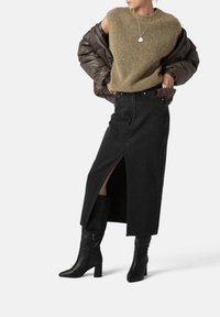 Brown puffer jacket over a green sleeveless top, paired with a black denim skirt featuring a front slit and black ankle boots. Silver necklace accent.