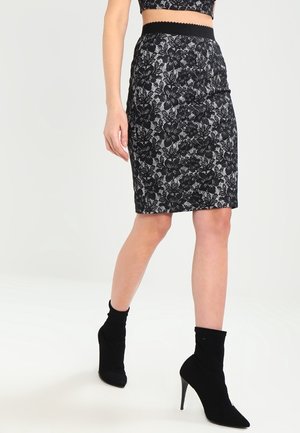 Schwarze Spitzen-Bleistiftrock mit floralem Muster, texturiertem Stoff und einem schwarzen elastischen Bund, kombiniert mit knöchelhohen schwarzen Stiefeln mit Absatz.