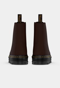 Botas de tobillo marrones con una textura suave, suela de goma negra, costuras amarillas y tiradores. Presentan un diseño de punta redonda.